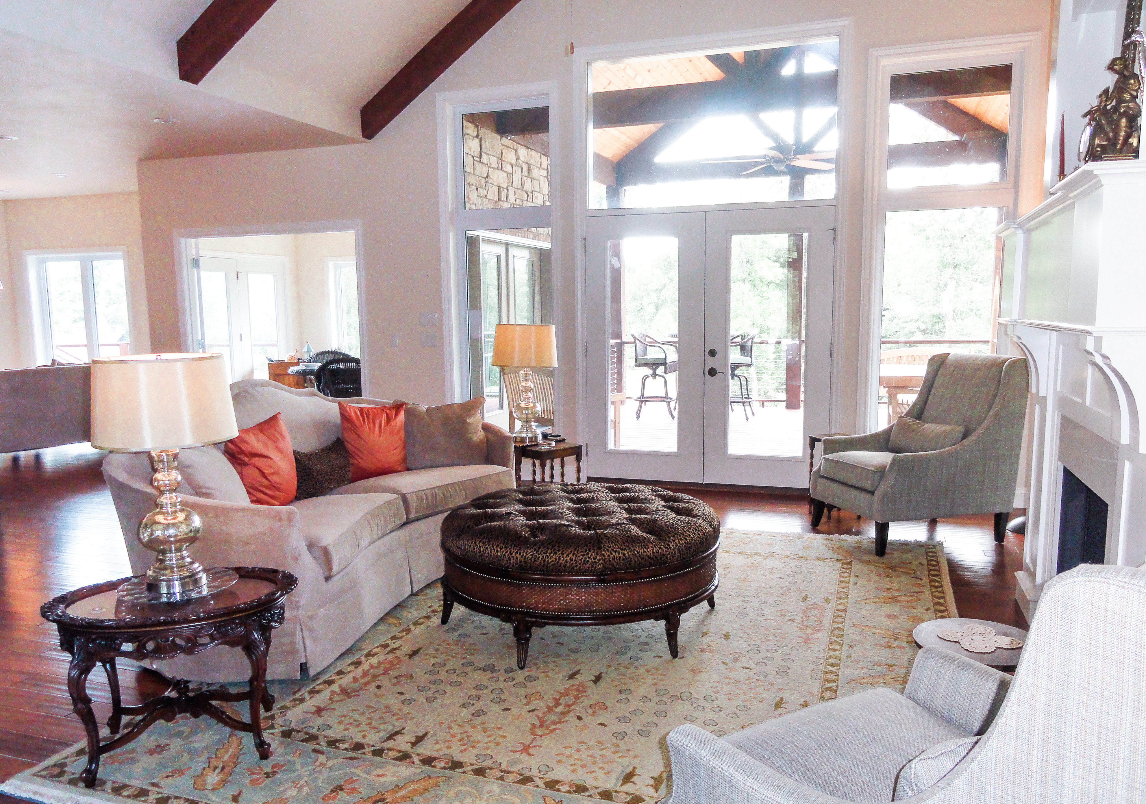 velvet couch, wood beams, white fireplace, wood floors, white mantle, french doors, round tufted ottoman,