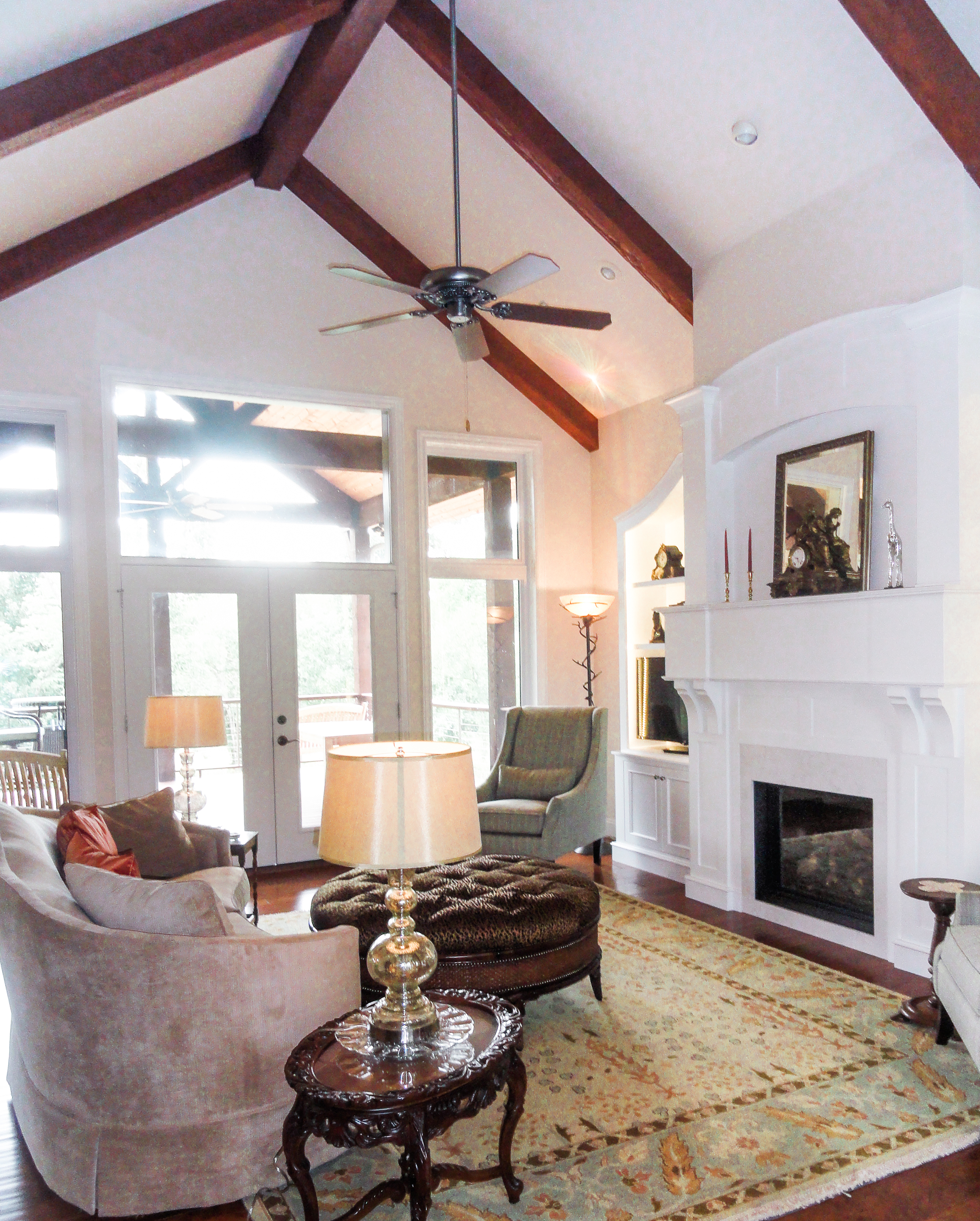 velvet couch, wood beams, white fireplace, white mantle, french doors, round tufted ottoman,