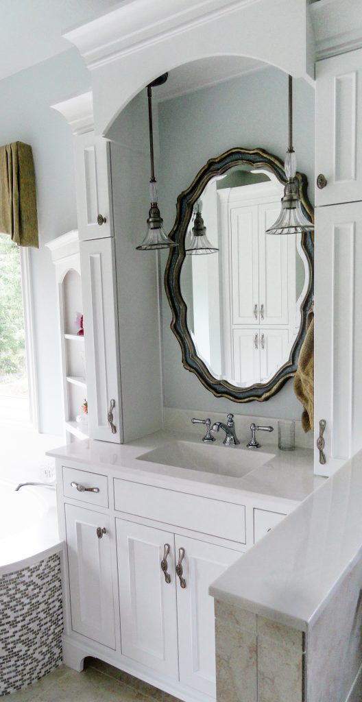 gold oval mirror, antique pendants, tile tub, white cabinets, bathroom sink