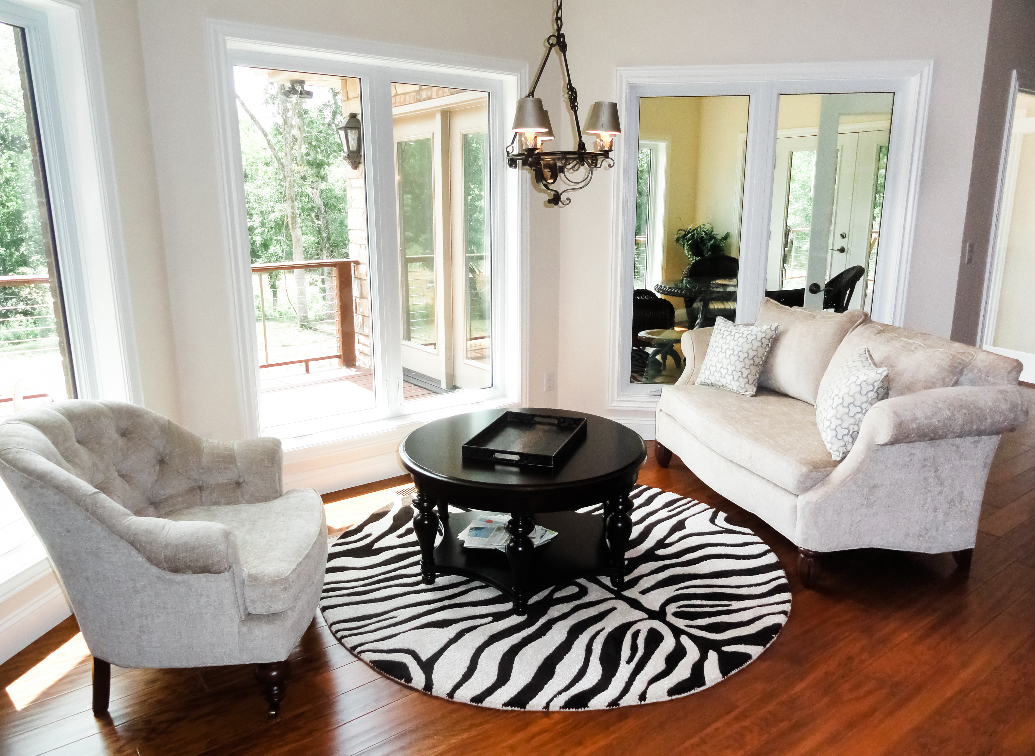 zebra round rug, ivory arm chair, ivory couch, black round coffee table, black serving tray, large windows, wood floors