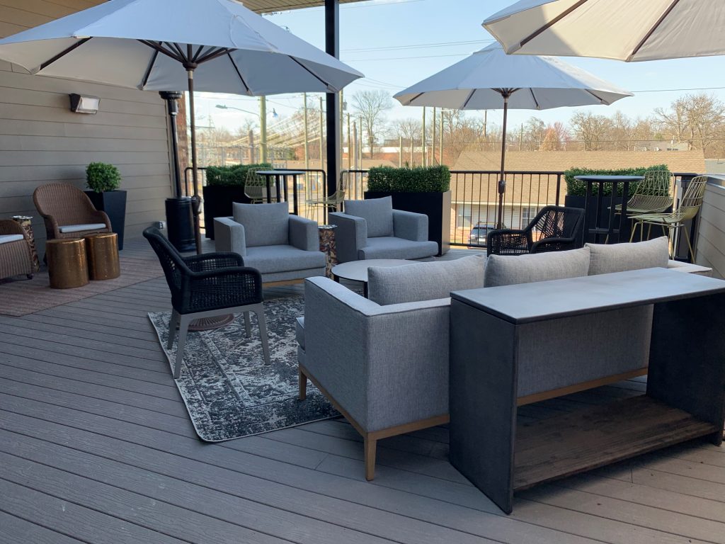 Cigar lounge, rooftop lounge, box hedge, greenery, umbrellas, bar height chairs, outdoor lounge, round metal table, grey outdoor couch, outdoor traditional rug, woven modern chairs, brass round tables, large metal sofa table