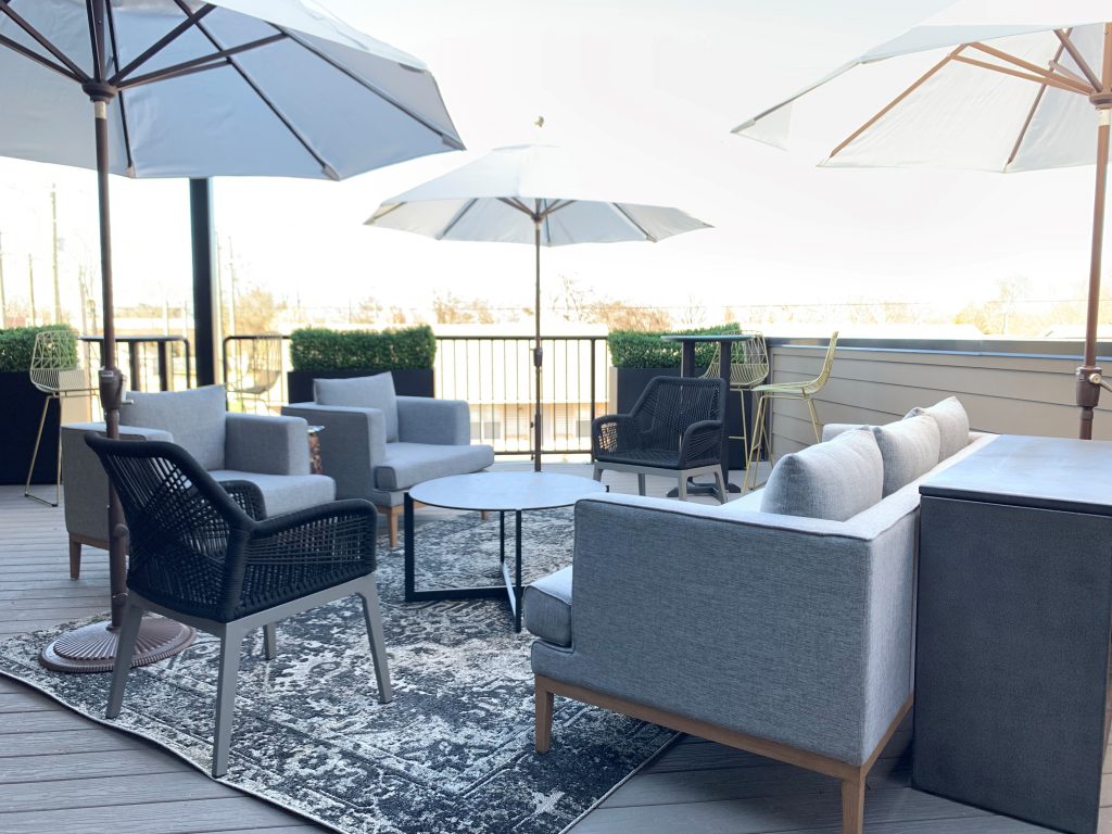 Cigar lounge, rooftop lounge, box hedge, greenery, umbrellas, bar height chairs, outdoor lounge, round metal table, grey outdoor couch, outdoor traditional rug, woven modern chairs