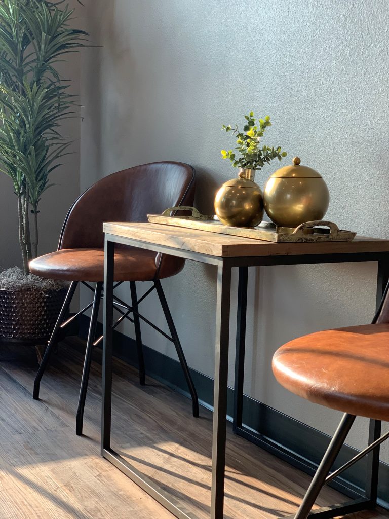 cigar lounge, comfortable leather chairs, rectangle center table, moody lighting, relaxing space,brass serving tray, table top greenery, tall greenery in corner, wood table, metal table legs, brass vase, brass bowl with lid