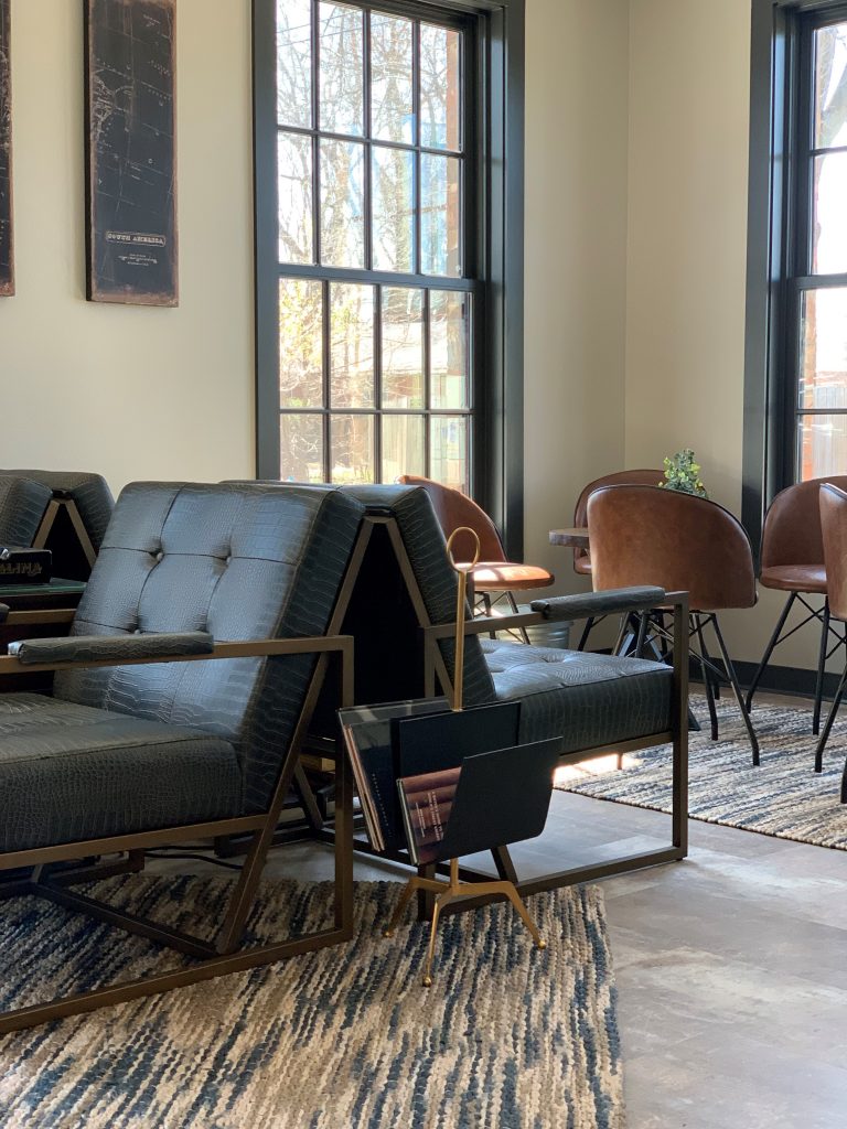 cigar lounge, conversation space, comfortable leather chairs, arm chair, moody lighting, relaxing space, woven rug, neutral color scheme, magazine holder, masculine, black framed windows